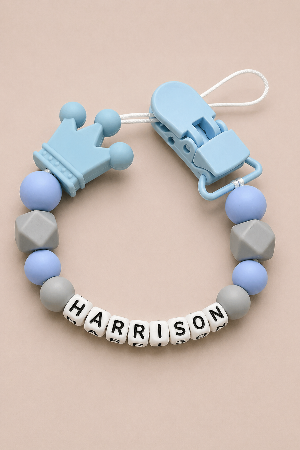 Baby teether with blue and gray beads and 'HARRISON' name tag on a beige background