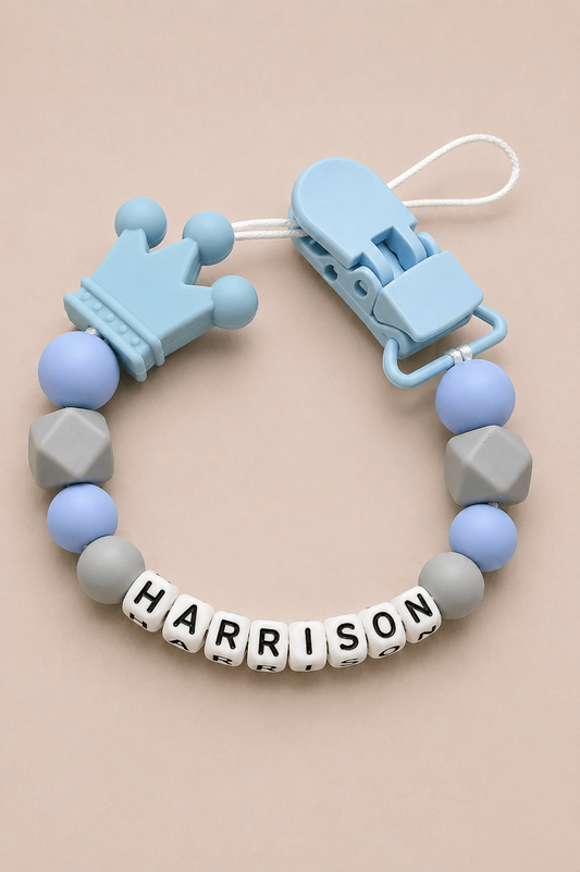 Baby teether with blue and gray beads and 'HARRISON' name tag on a beige background