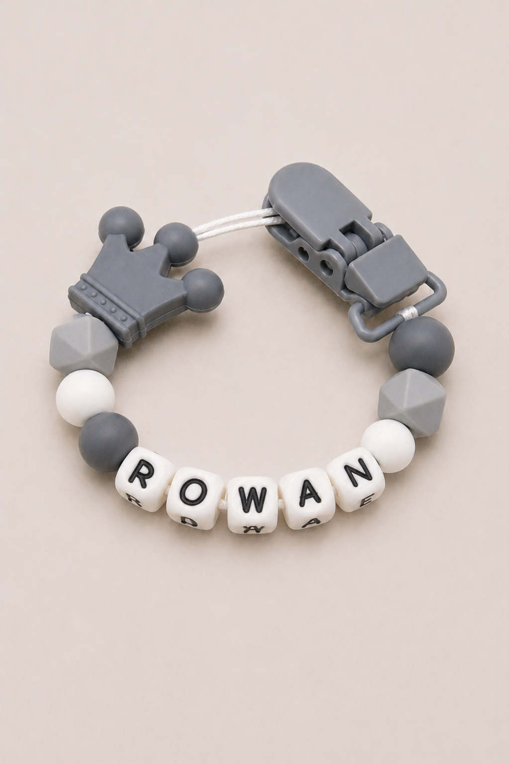 Teething bracelet with geometric beads and letter tiles spelling 'ROWAN' on a beige background