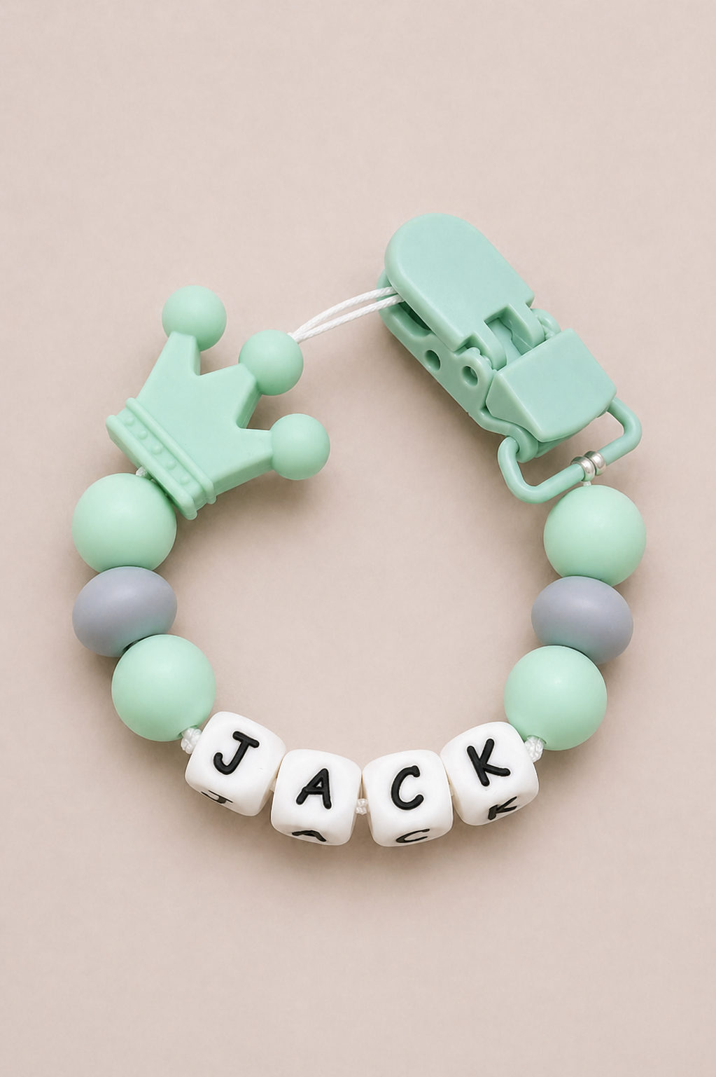Mint green baby teether with 'JACK' on a beige background
