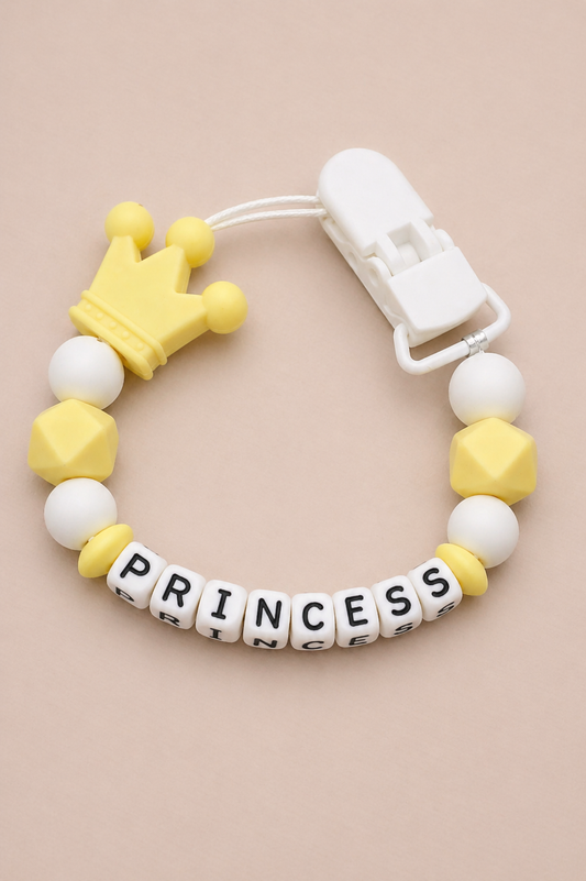 Teething bracelet with yellow crown, white beads, and 'PRINCESS' letters on a beige background