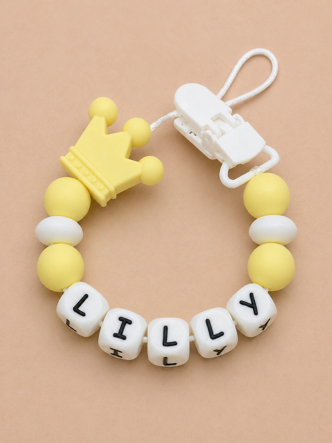 Yellow and white teething ring with 'LILLY' on a beige background