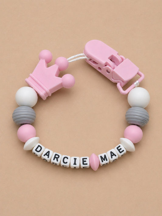 Baby teether with colorful beads and a crown-shaped clip on a beige background