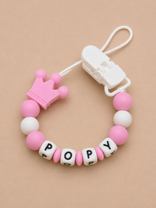 Pink and white pacifier clip with letter beads on a beige background
