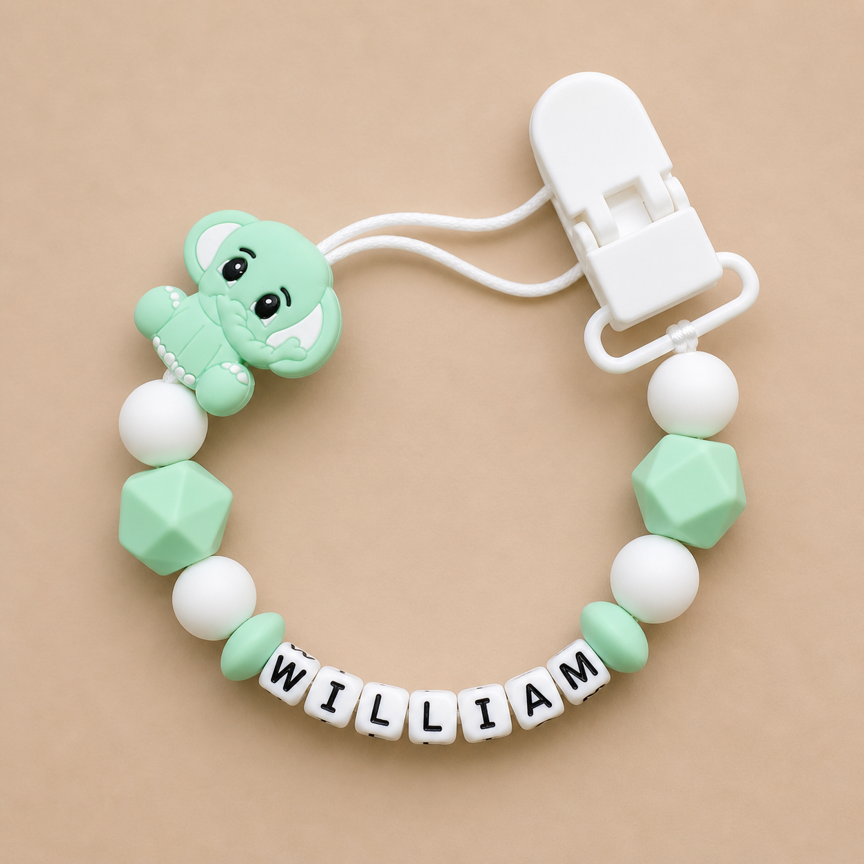 dummy clip with green dinosaur design and 'WILLIAM' letters on a beige background