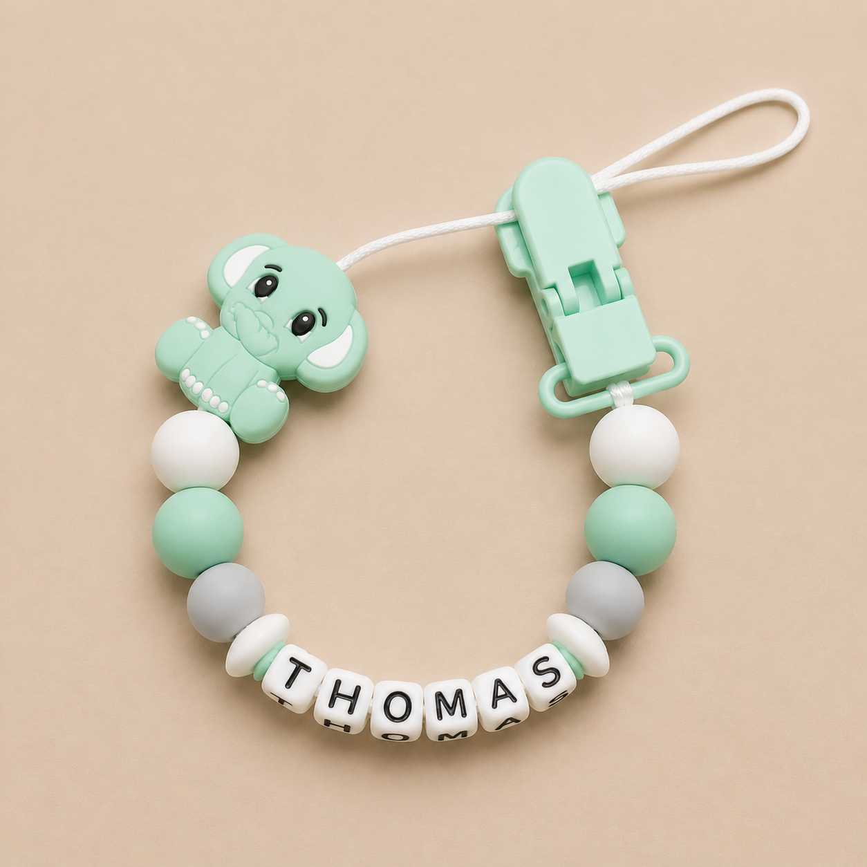 Mint green dummy clip with name 'THOMAS' on a beige background