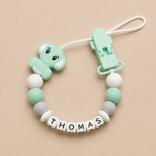 Mint green dummy clip with name 'THOMAS' on a beige background