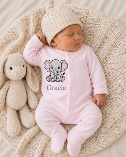 Newborn baby in a pink onesie with an elephant design and 'Gracie' text, lying on a textured blanket next to a plush toy.