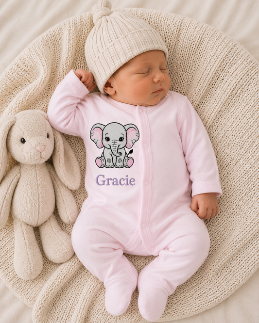 Newborn baby in a pink onesie with an elephant design and 'Gracie' text, lying on a textured blanket next to a plush toy.