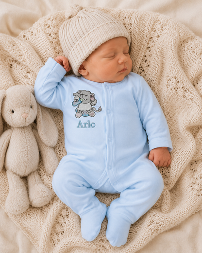 Newborn baby in a blue onesie with a teddy bear design and 'Arlo' text, wearing a beige knit hat, lying on a textured beige blanket with a plush toy beside.