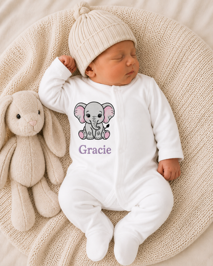 Newborn baby in a white onesie with an elephant design and 'Gracie' text, next to a plush toy on a textured surface.