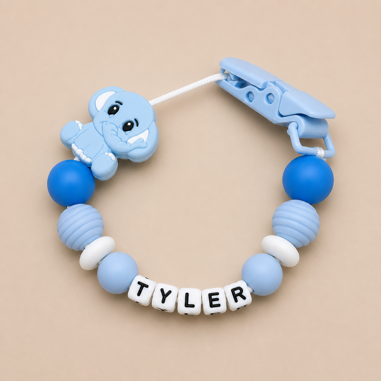 Blue baby dummy clip with a clip and 'TYLER' name beads on a beige background