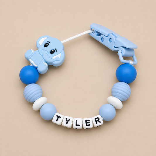 Blue baby dummy clip with a clip and 'TYLER' name beads on a beige background
