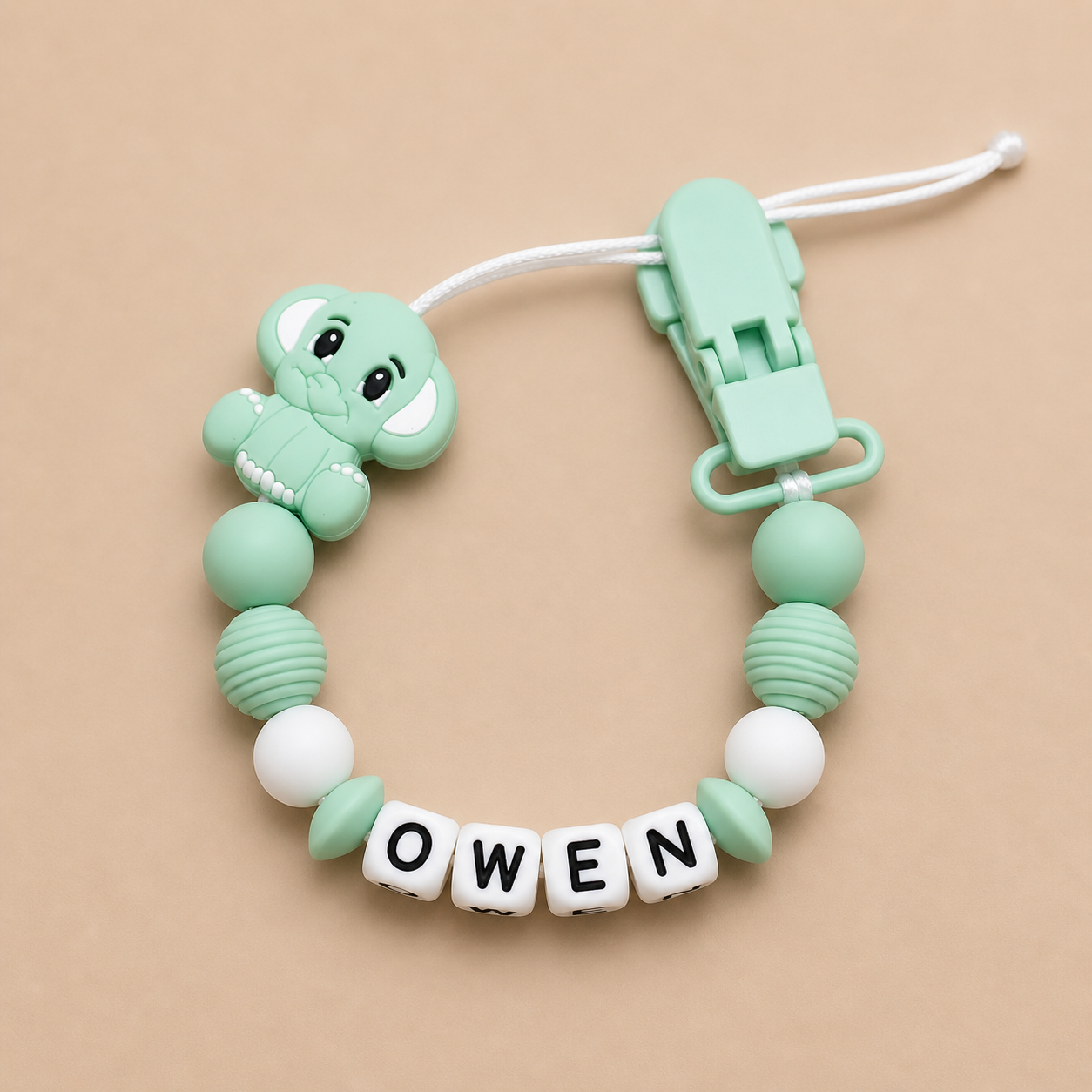 Mint green dummy clip with 'OWEN' letters on a beige background