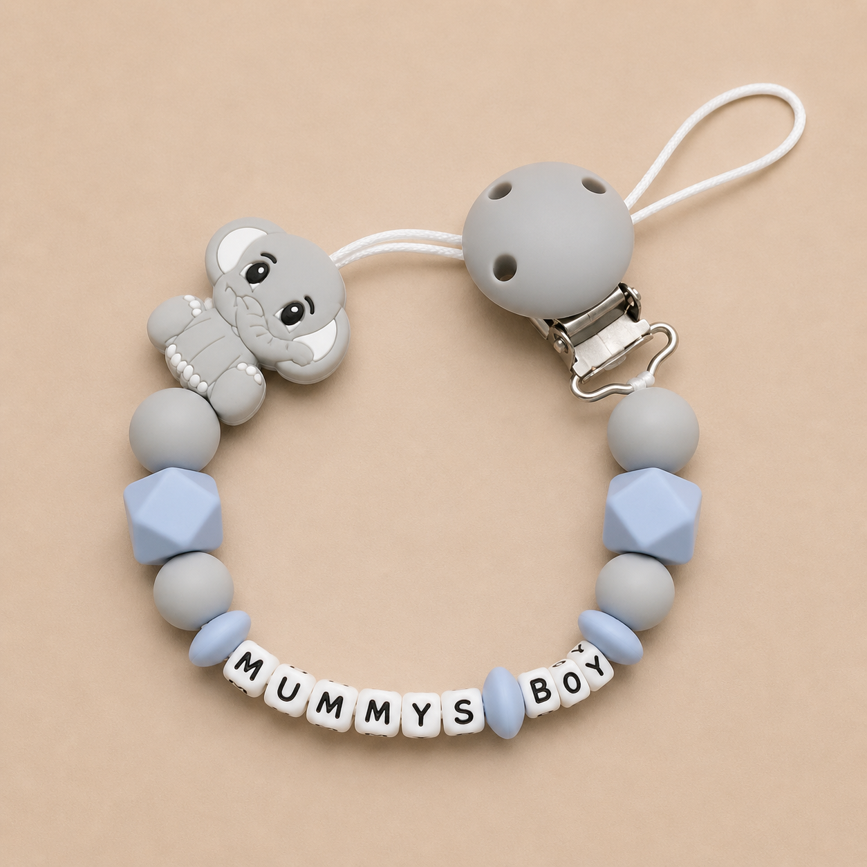 Silicone dummy clip with 'MUMMYS BOY' letter beads on a beige background