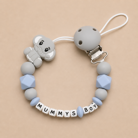 Silicone dummy clip with 'MUMMYS BOY' letter beads on a beige background