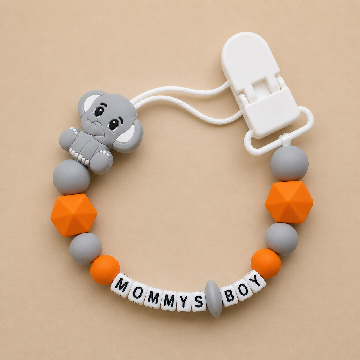 dummy clip with elephant charm, colorful beads, and 'MOMMY'S BOY' tag on a beige background
