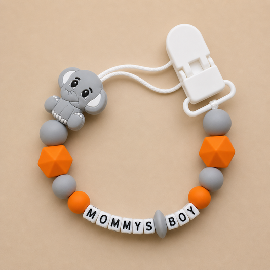 dummy clip with elephant charm, colorful beads, and 'MOMMY'S BOY' tag on a beige background