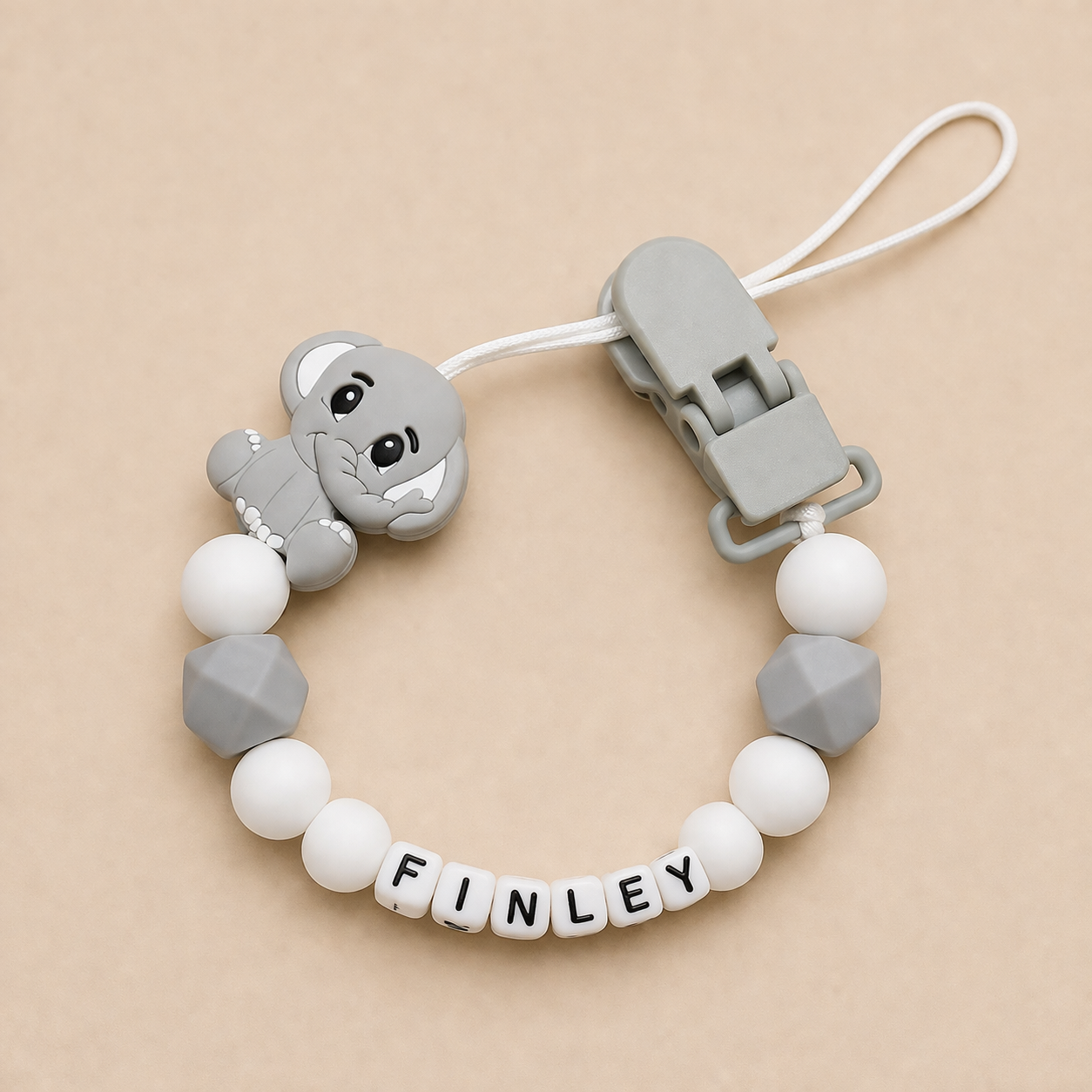 dummy clip with elephant charm and 'FINLEY' beads on a beige background