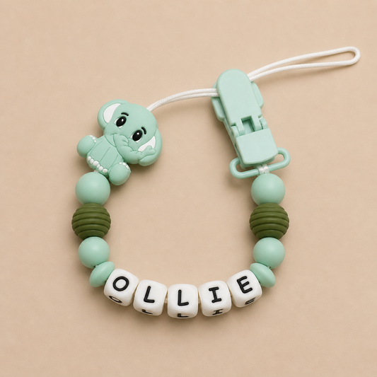 Mint green dummy clip with a elephant charm and letter beads on a beige background