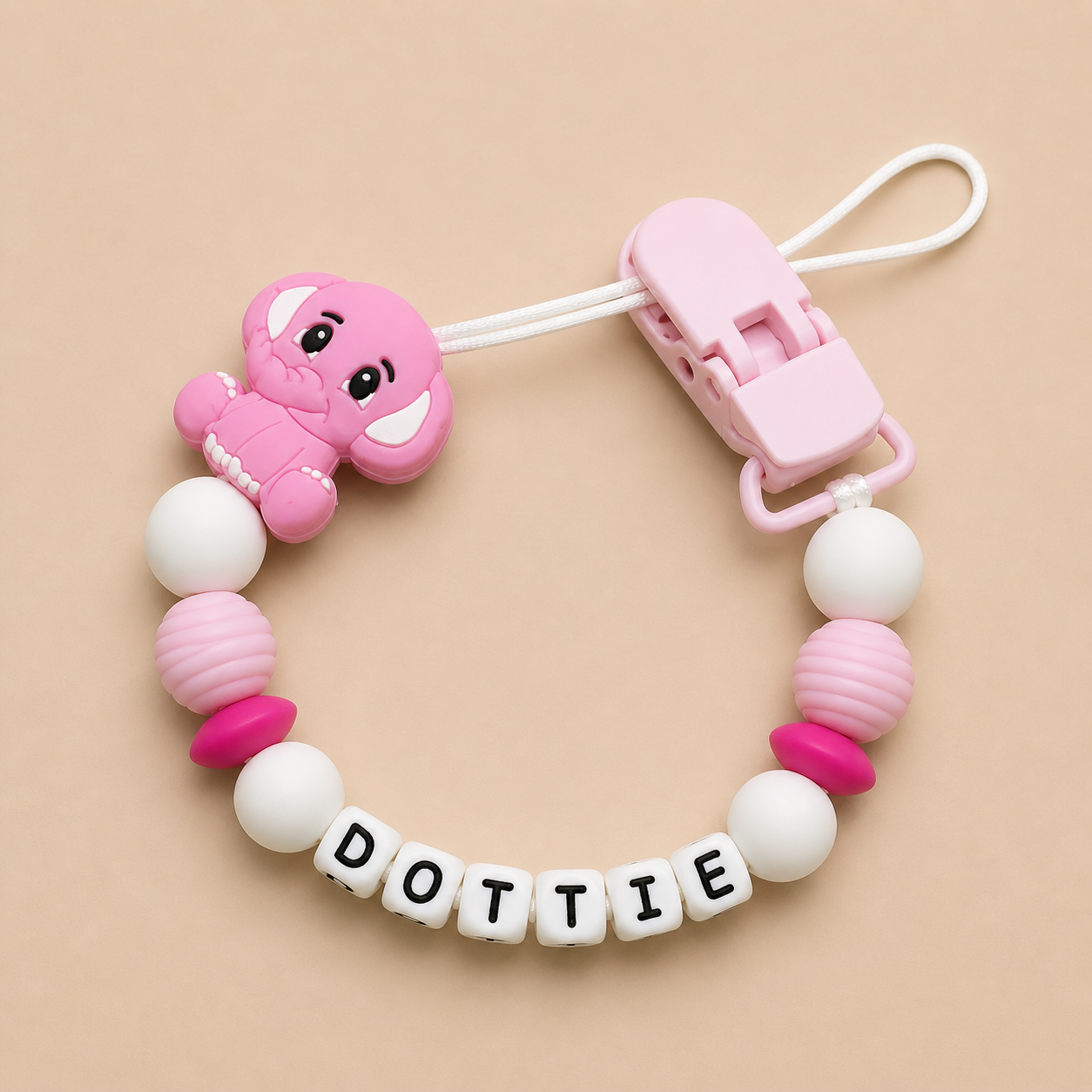 Pink and white baby dummy clip with 'DOTTIE' on a beige background