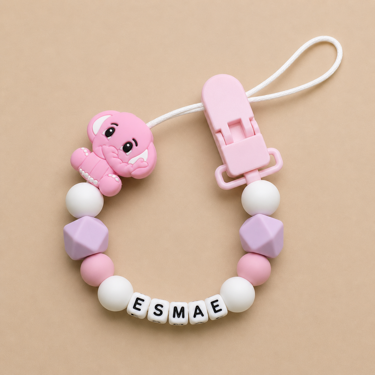 Pink baby dummy clip with a clip and 'ESMAE' beads on a beige background