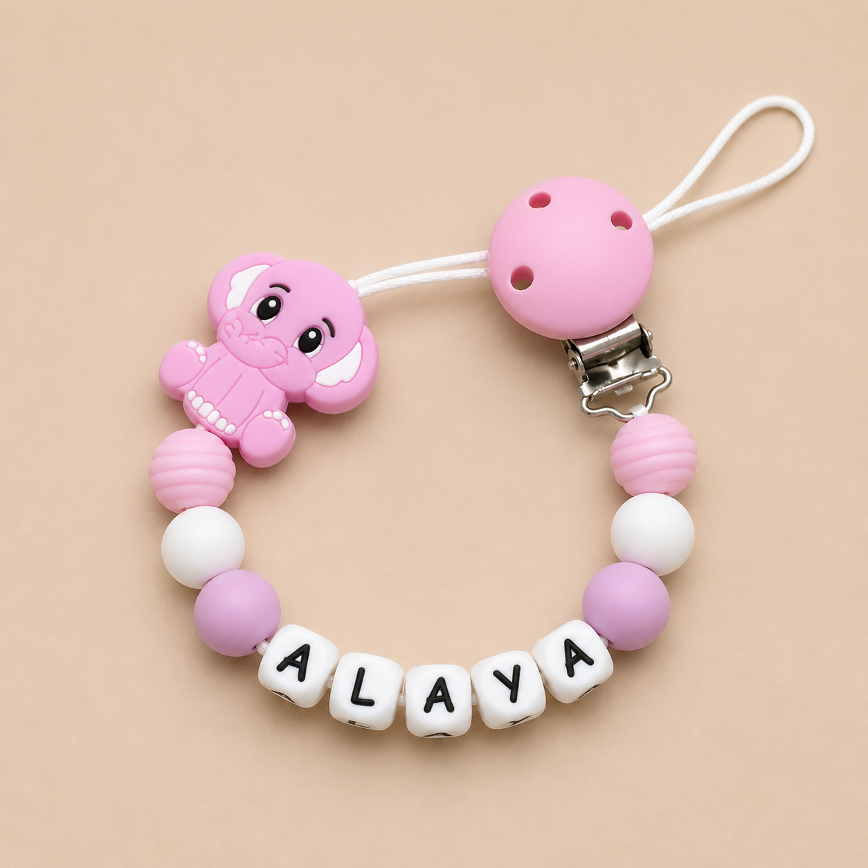 Pink baby teether with 'ALAYA' on a beige background