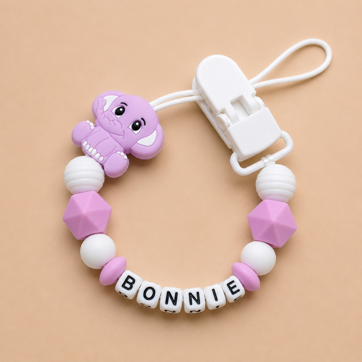 dummy clip with a purple elephant charm and 'BONNIE' letter beads on a beige background