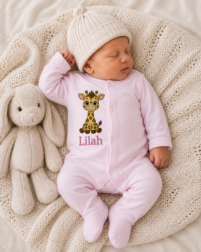 Newborn baby in a pink onesie with a giraffe design and 'Lilah' text, lying on a textured blanket with a plush toy.