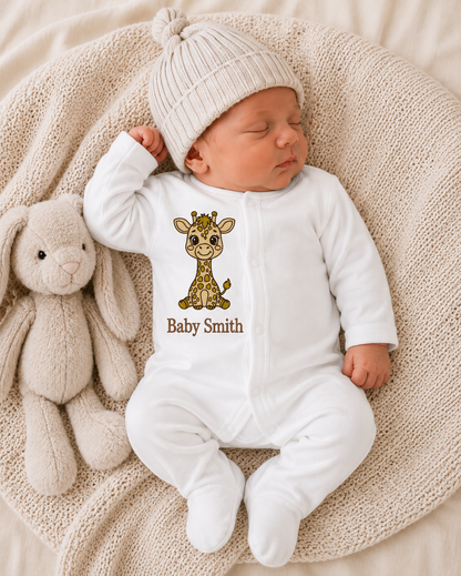 Newborn baby in a white onesie with a giraffe design and 'Baby Smith' text, lying on a soft surface next to a plush toy.