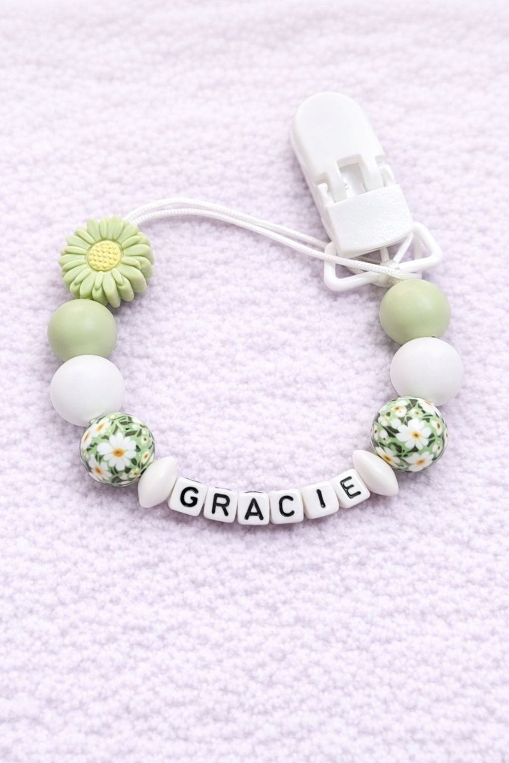 Dummy Clip with floral beads and 'GRACIE' charm on a light purple textured background
