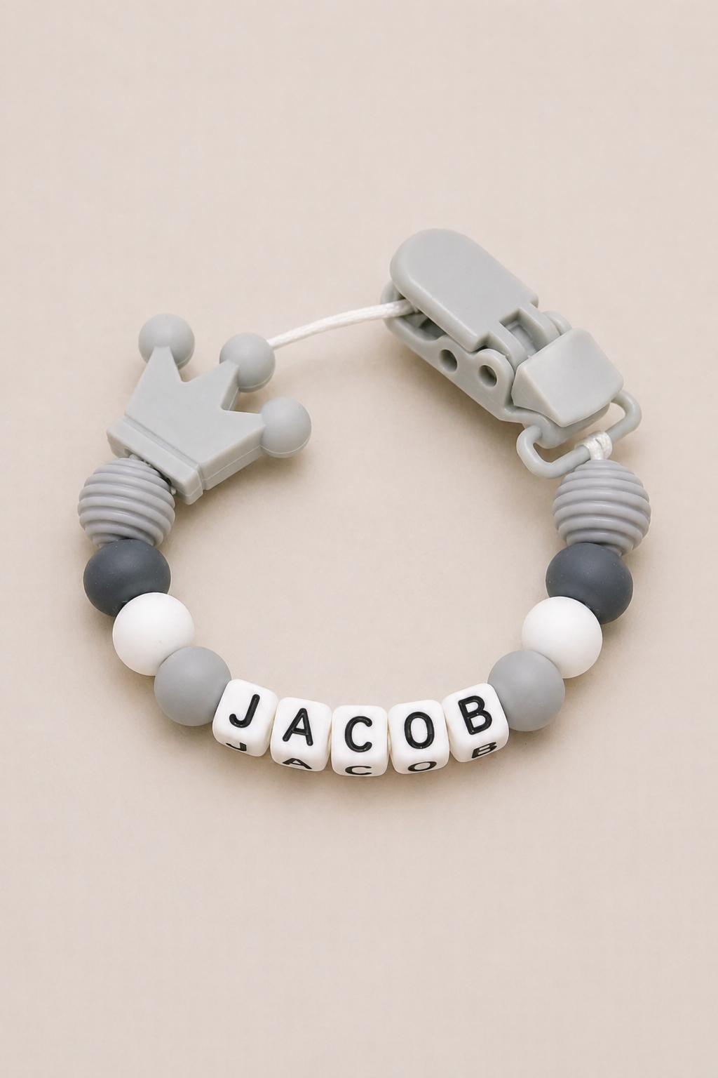 Teething bracelet with gray and white beads and a crown charm on a beige background