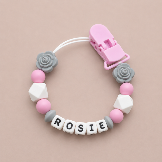 Baby dummy clip with colorful beads and a pink clip on a beige background
