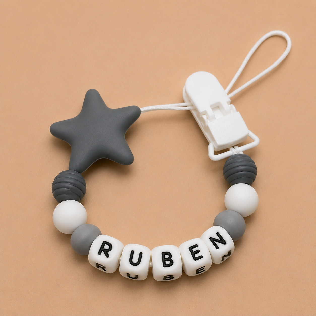 dummy clip with star-shaped chewable and letter beads spelling 'RUBEN' on a beige background