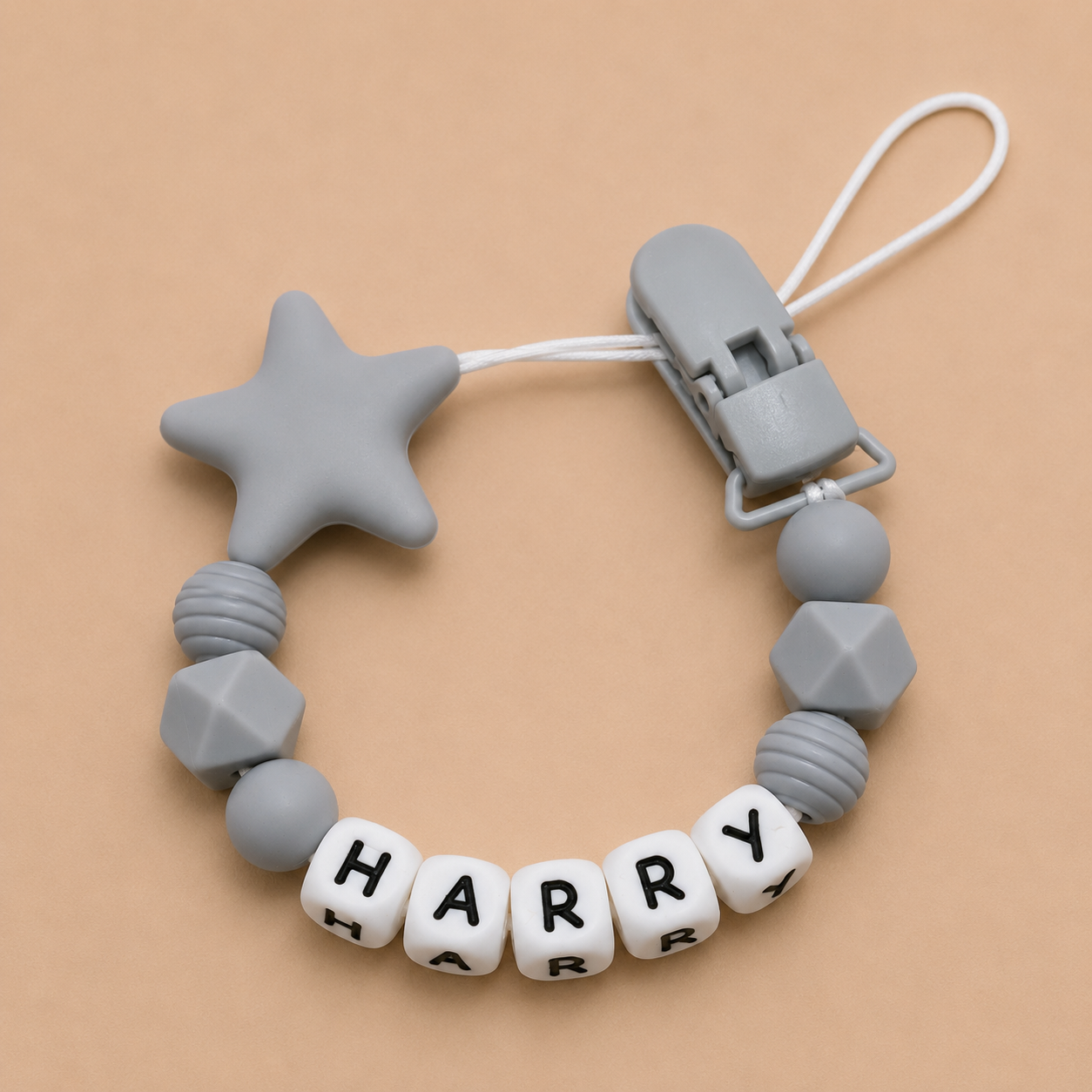 Gray dummy clip with star-shaped bead and letter beads spelling 'HARRY' on a beige background