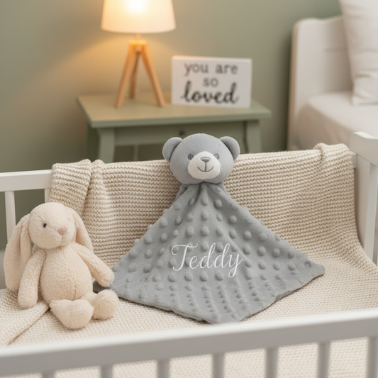 Personalised grey teddy bear baby comforter with dimple minky body, embroidered with a name in a nursery setting