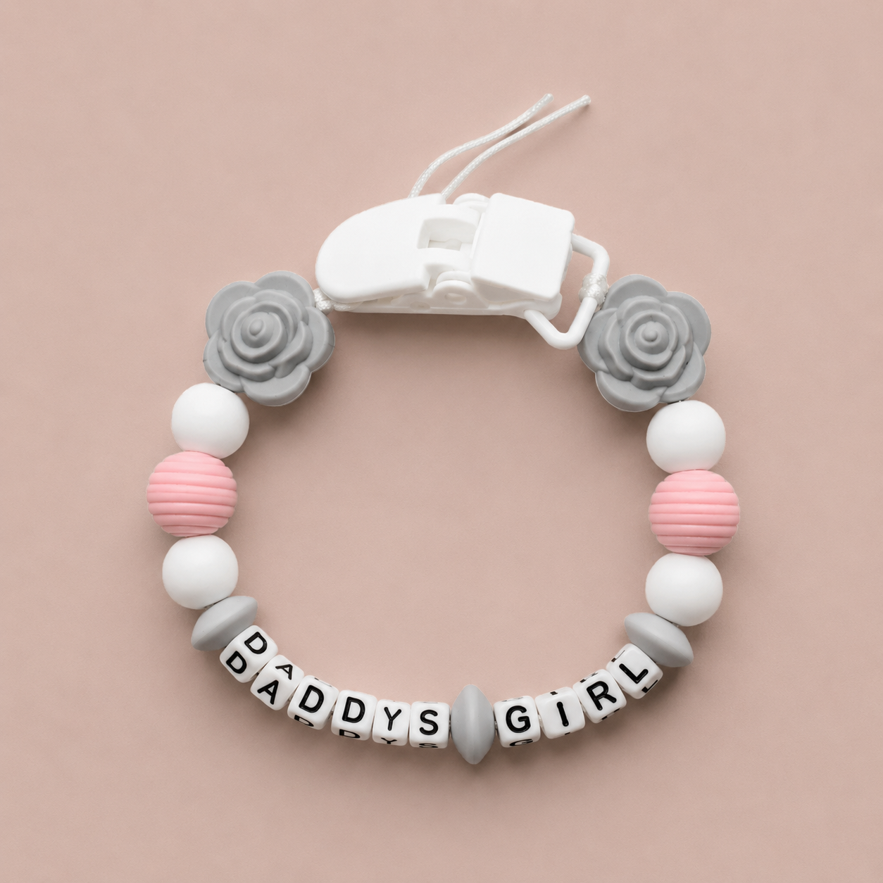 Baby dummy clip with 'DADDYS GIRL' beads on a beige background