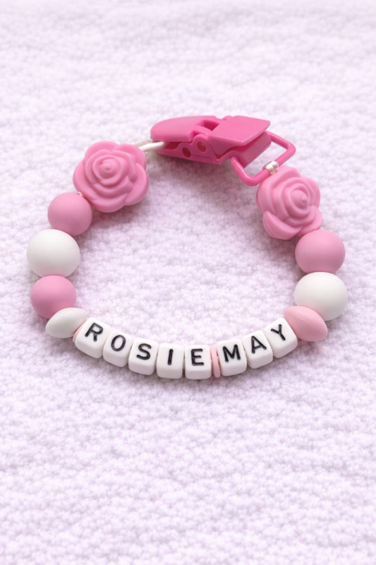 Pink and white teething dummy clip with 'ROSIE MAY' on a pink textured background