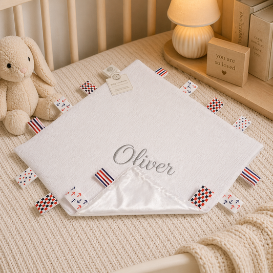 Baby blanket with 'Oliver' embroidered on it, surrounded by toys and decor in a crib.