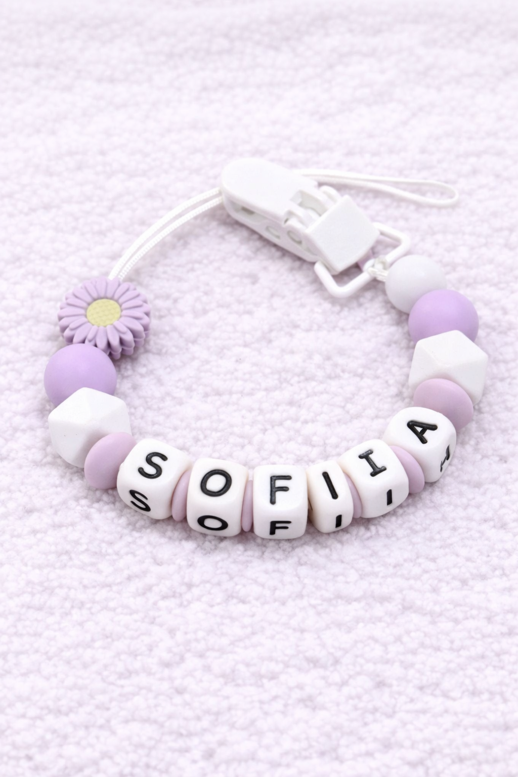 dummy clip with letter beads spelling 'SOFIA' on a light purple textured background