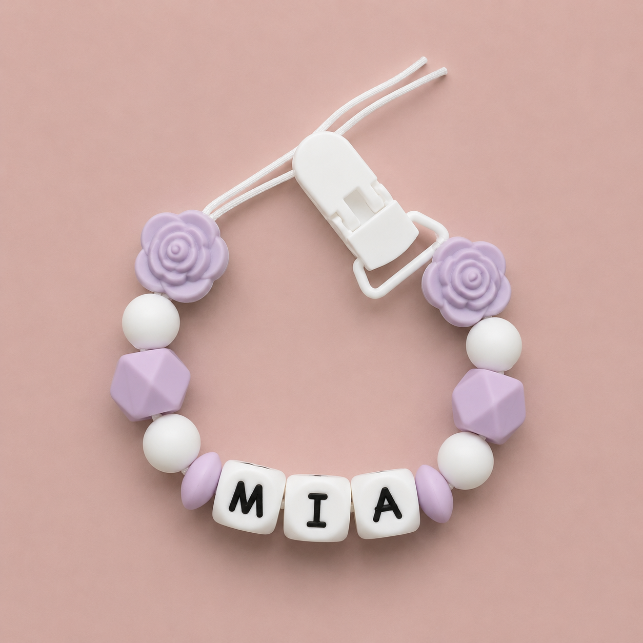 Baby Dummy Clip with purple and white beads and letter tiles spelling 'MIA' on a pink background