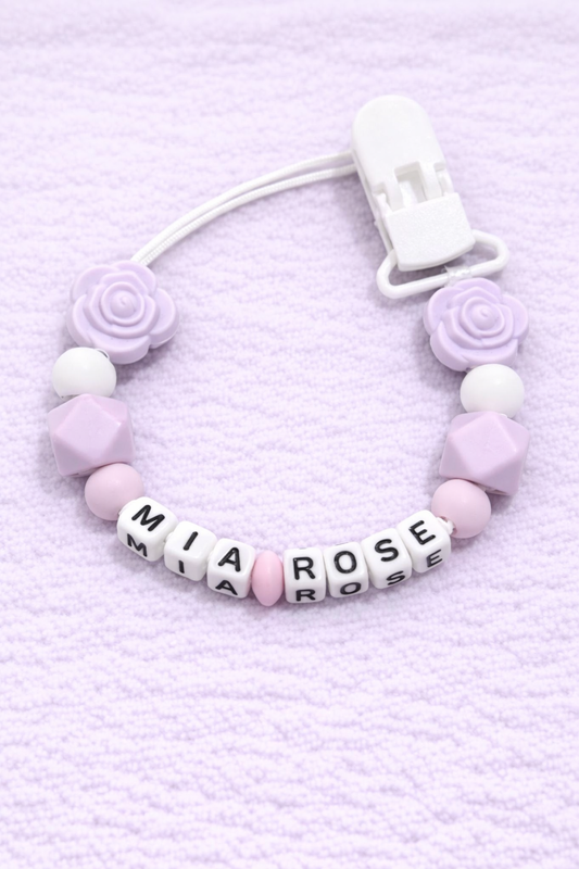 Pacifier clip with pink and white beads and letter beads spelling 'Mia Rose' on a light purple background