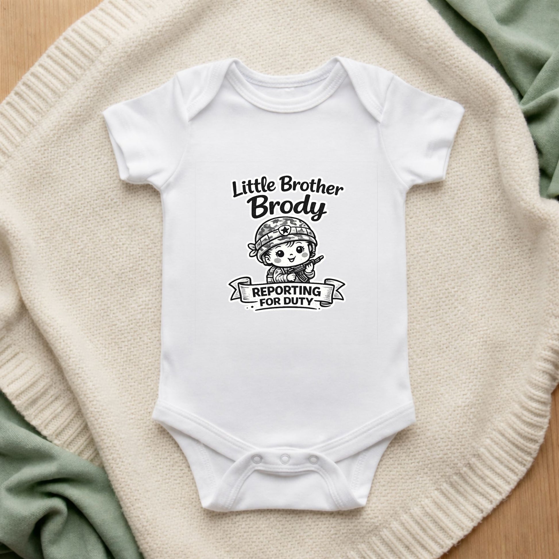 White baby onesie with 'Little Brother Brody Reporting for Duty' text and graphic on a textured surface.