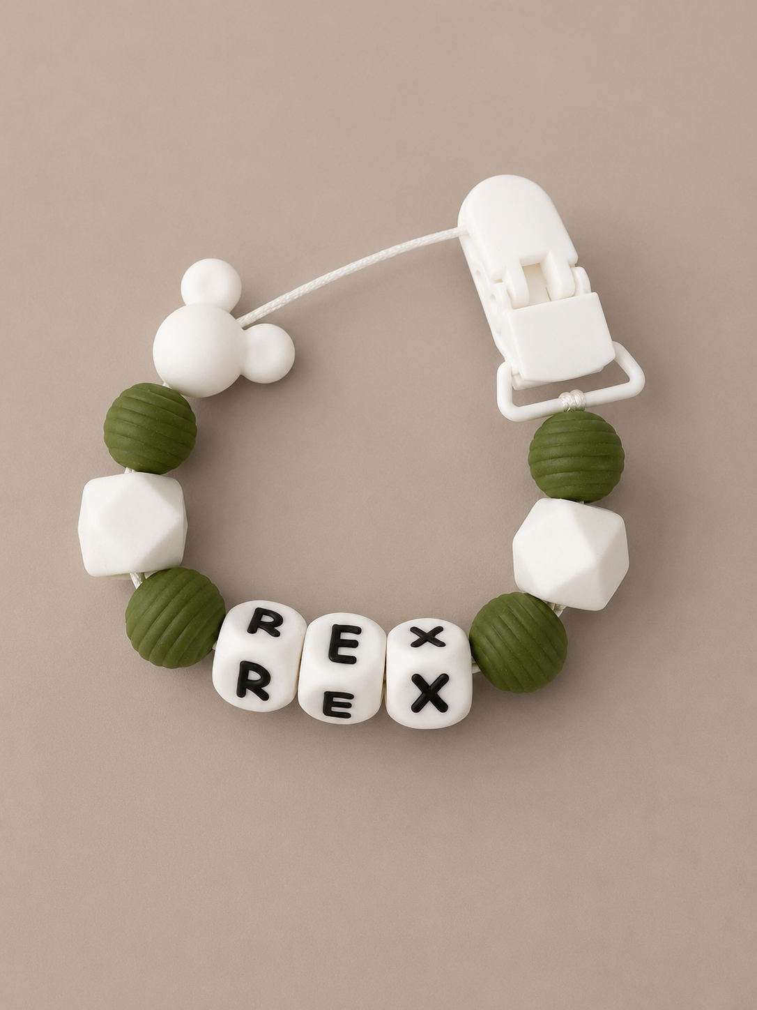 A baby teething bracelet with olive green and white silicone beads, featuring three letter beads spelling 'REX' and a white Mickey Mouse-shaped bead, shown on a neutral beige background.