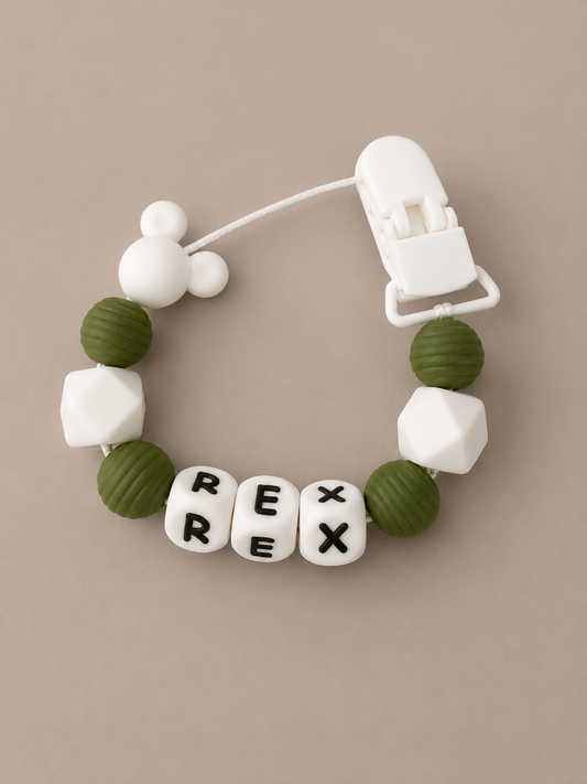 A baby teething bracelet with olive green and white silicone beads, featuring three letter beads spelling 'REX' and a white Mickey Mouse-shaped bead, shown on a neutral beige background.