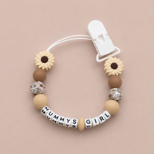 Beaded pacifier clip with 'MUMMY'S GIRL' beads on a beige background