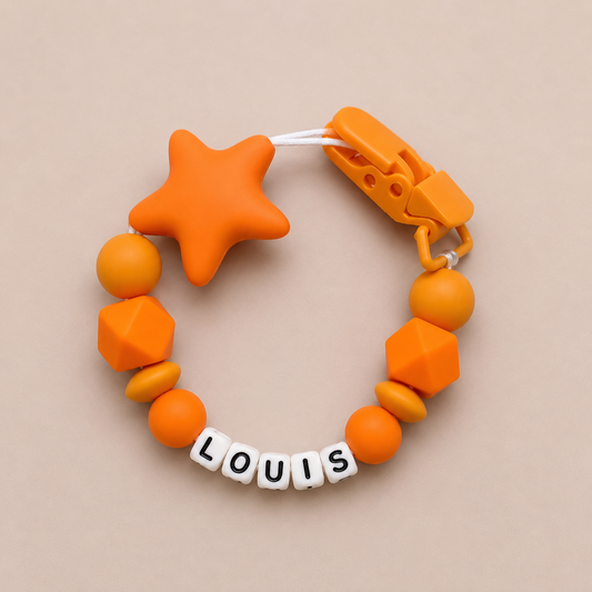 Orange baby dummy clip with geometric shapes and a clip on a beige background