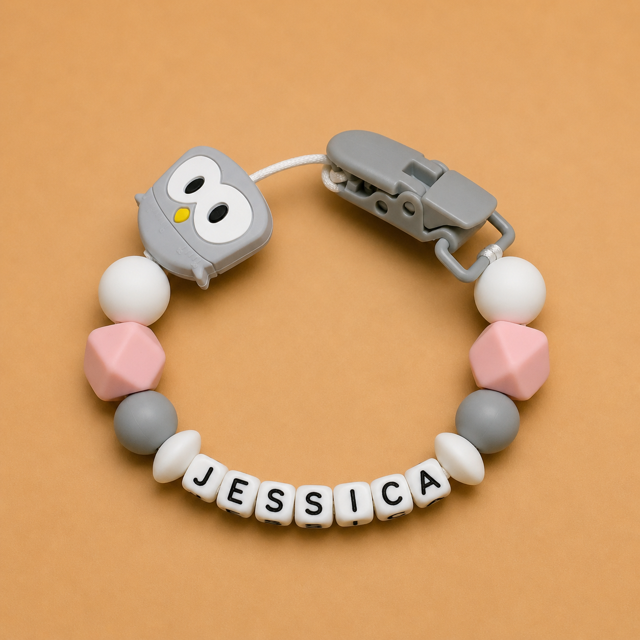 Baby dummy clips with colorful beads and 'JESSICA' letter beads on a brown background
