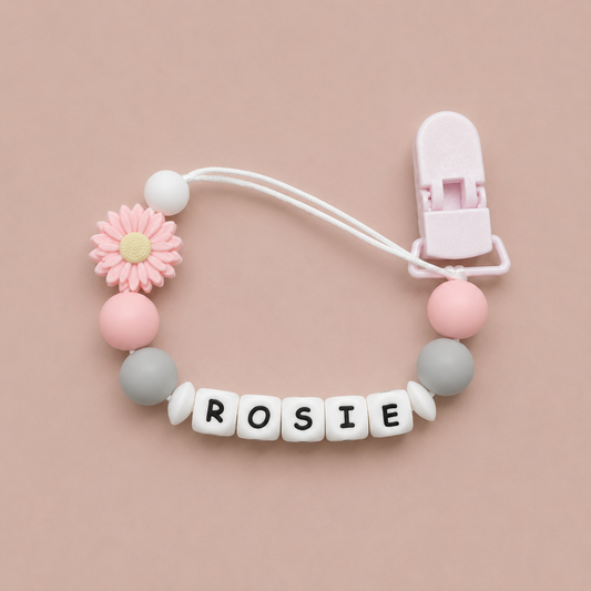 Baby dummy clip with colorful beads and a clip on a pink background