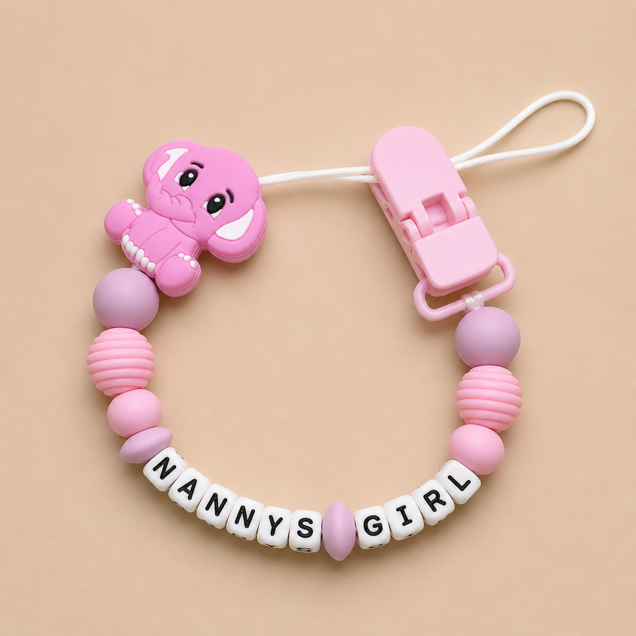 Pink baby dummy clip with 'NANNY'S GIRL' letters on a beige background